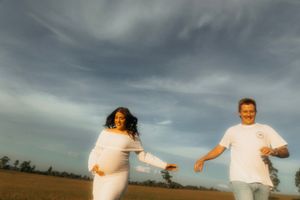Two people in white clothing run joyfully across a field under dramatic cloudy skies at dusk.