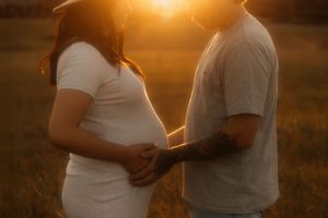 Silhouetted couple shares an intimate moment during sunset as they touch a pregnant belly in golden light.