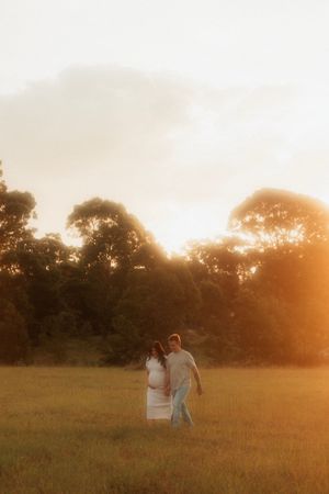 Silhouettes of a couple standing in a golden meadow at sunset with trees in the background creating a warm atmosphere.