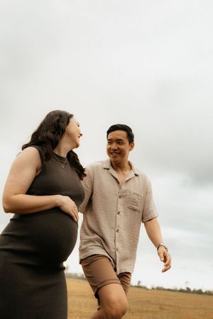 A couple sharing a joyful moment together while standing in an open field against an overcast sky.
