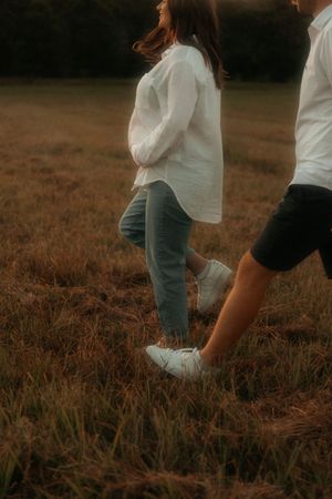 Couple in white shirts and jeans walk through a dusky meadow with moody atmospheric lighting.