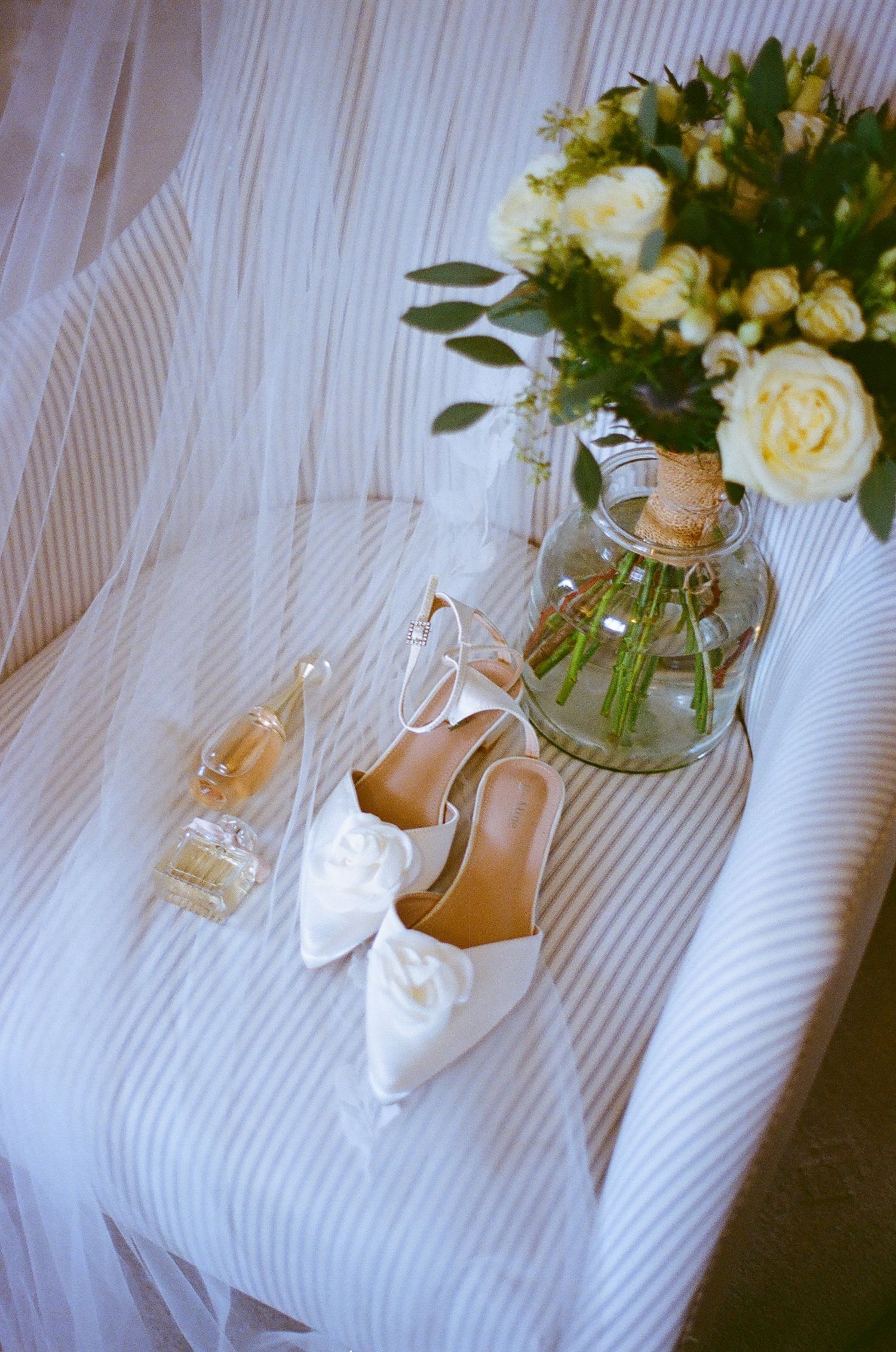 Elegant white bridal shoes and floral arrangements displayed on a striped fabric background.