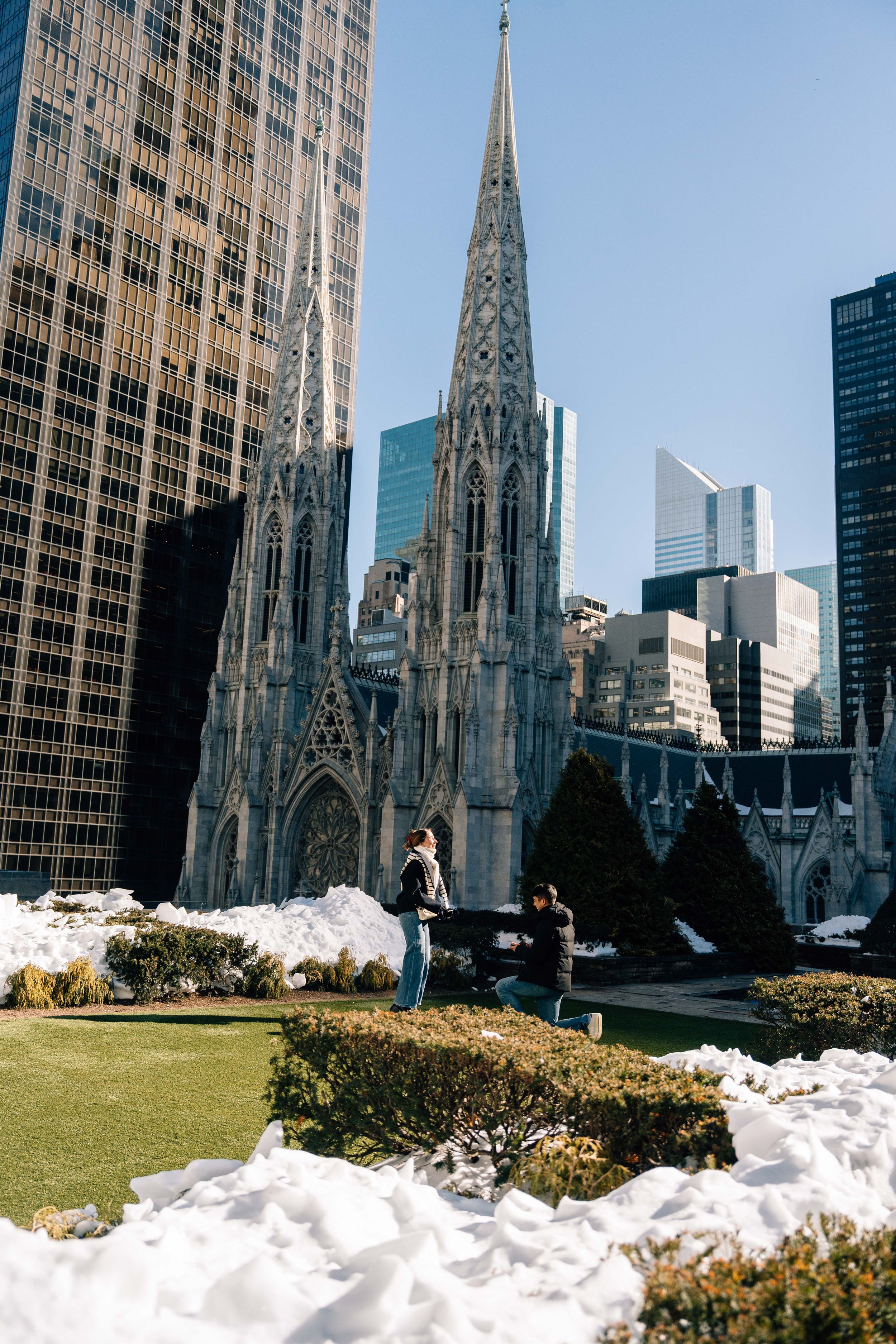 Snow covers the rooftop garden at Rockefeller Center with St. Patrick's Cathedral spires visible in New York City.