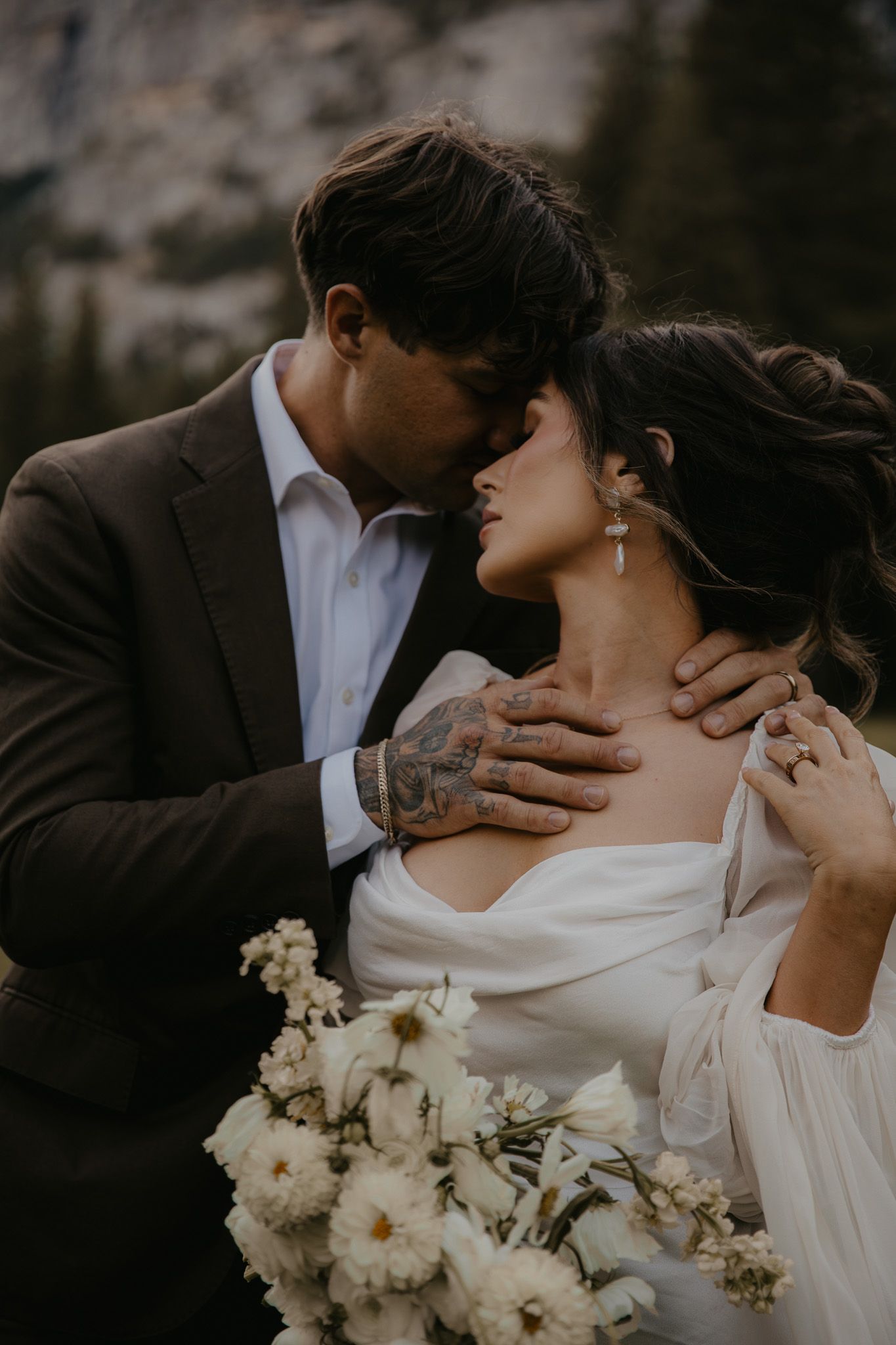 Intimate wedding portrait of couple with white bouquet against dramatic mountain backdrop.