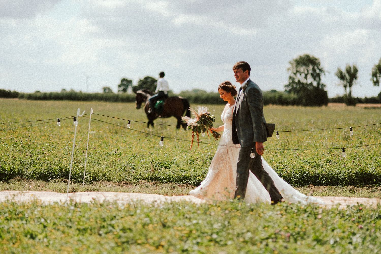 Bride and groom walk through a sunny field with wildflowers.
