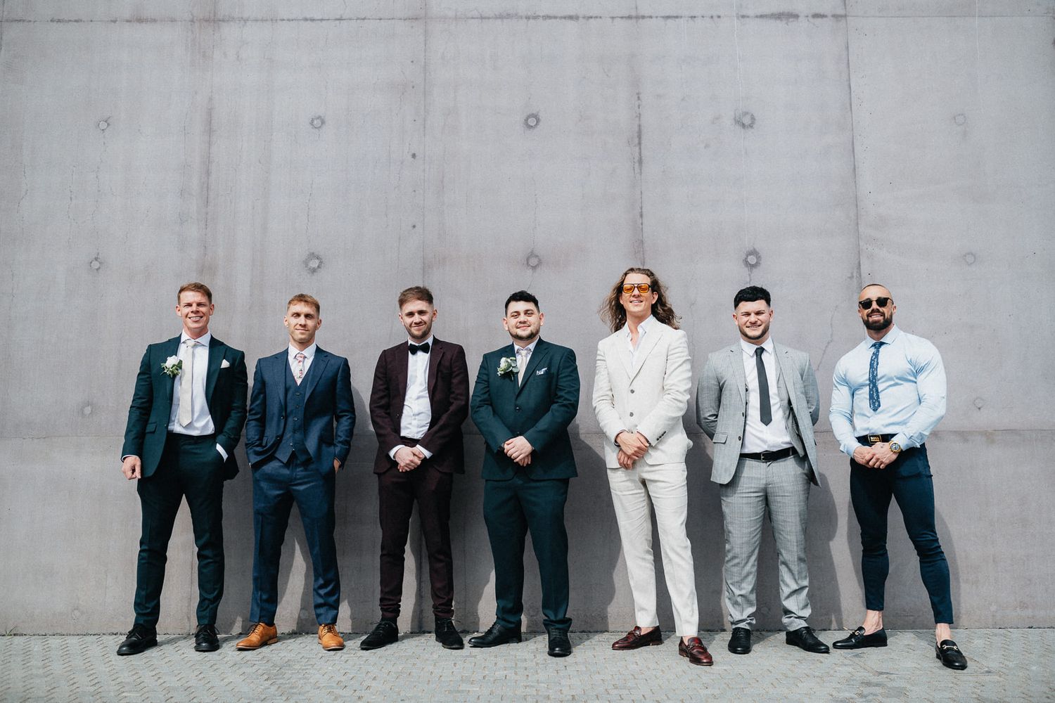 Wedding party in stylish suits posing against modern concrete wall background.