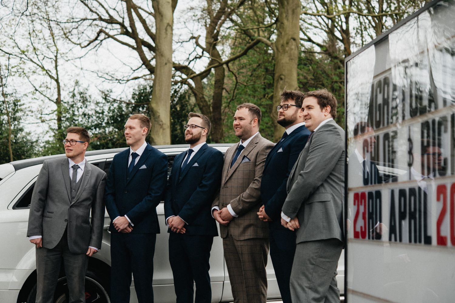 Groomsmen in classic suits lined up outdoors for formal wedding portraits.