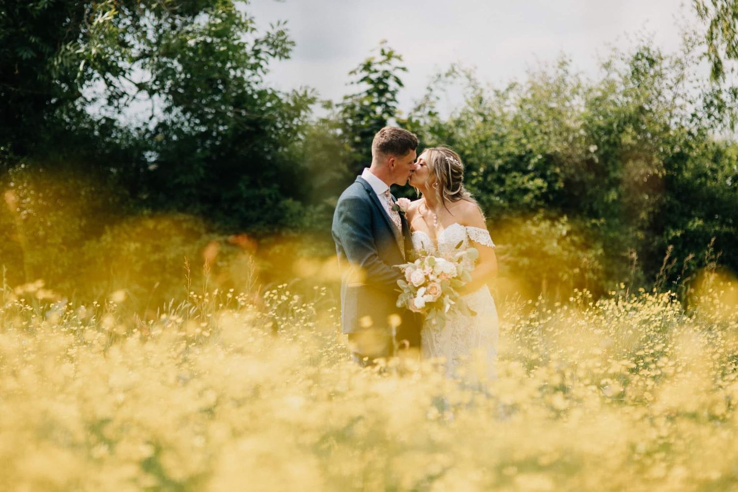 Newlyweds share an intimate moment in a sunlit field of golden wildflowers.