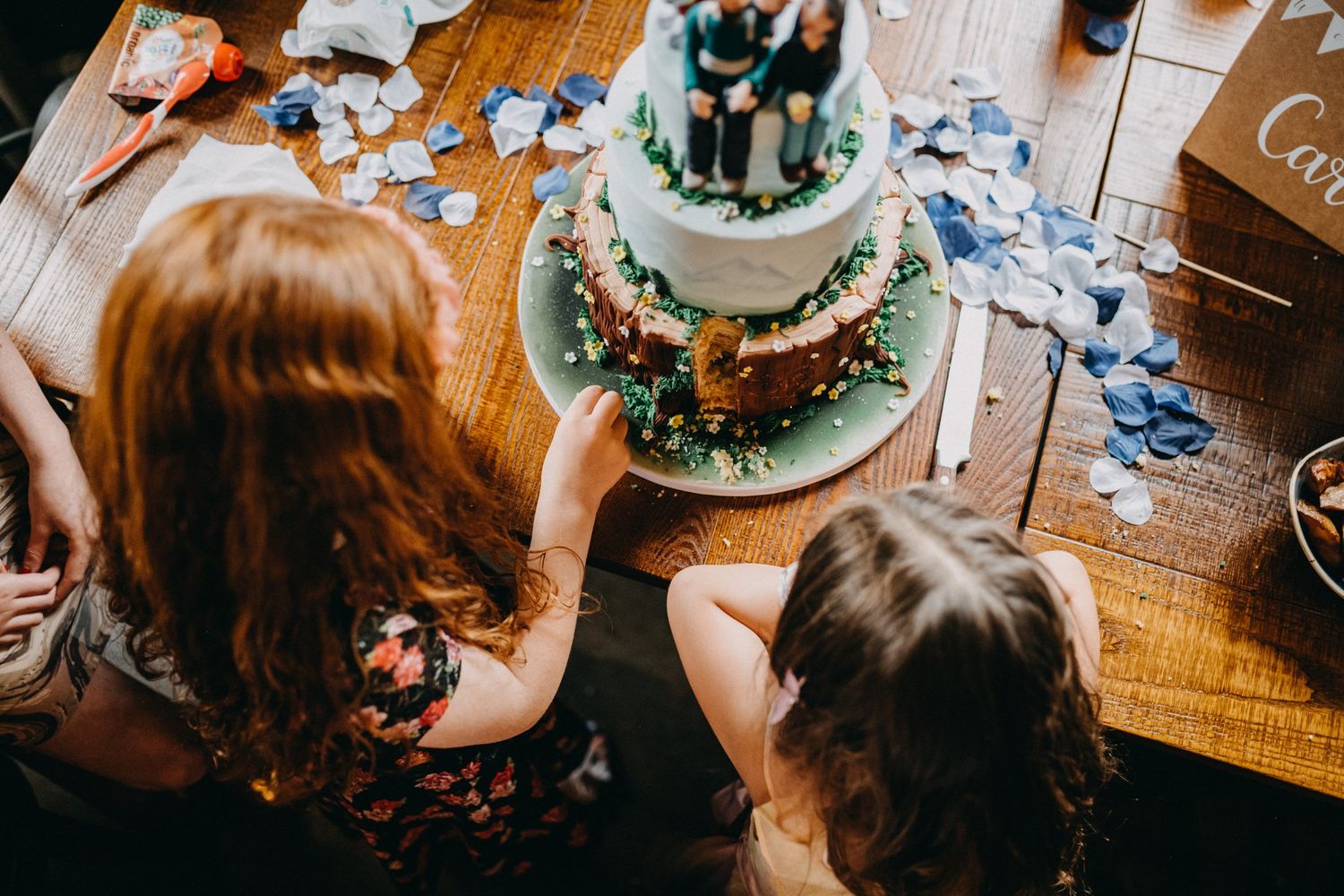 Overhead view of wedding cake being admired at reception with decorative table setting.