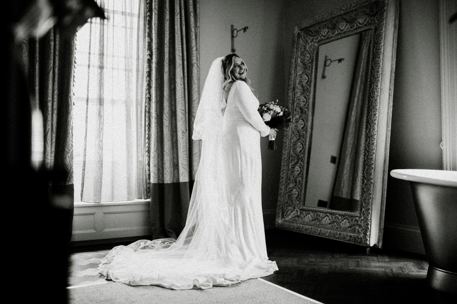 A flowing white wedding dress train elegantly draped near a window in dramatic black and white.