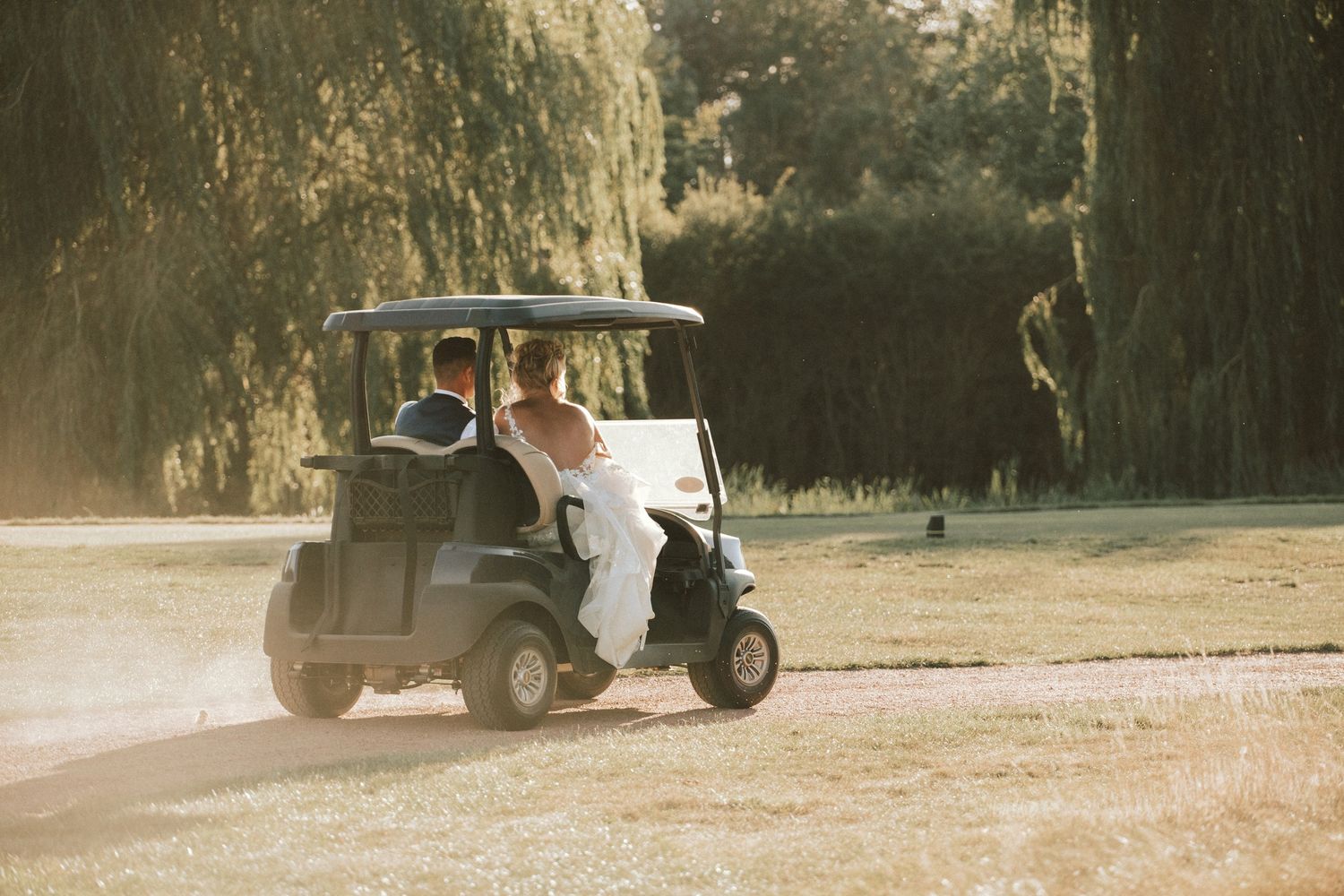 A golf cart drives across a sun-drenched field during a wedding day.