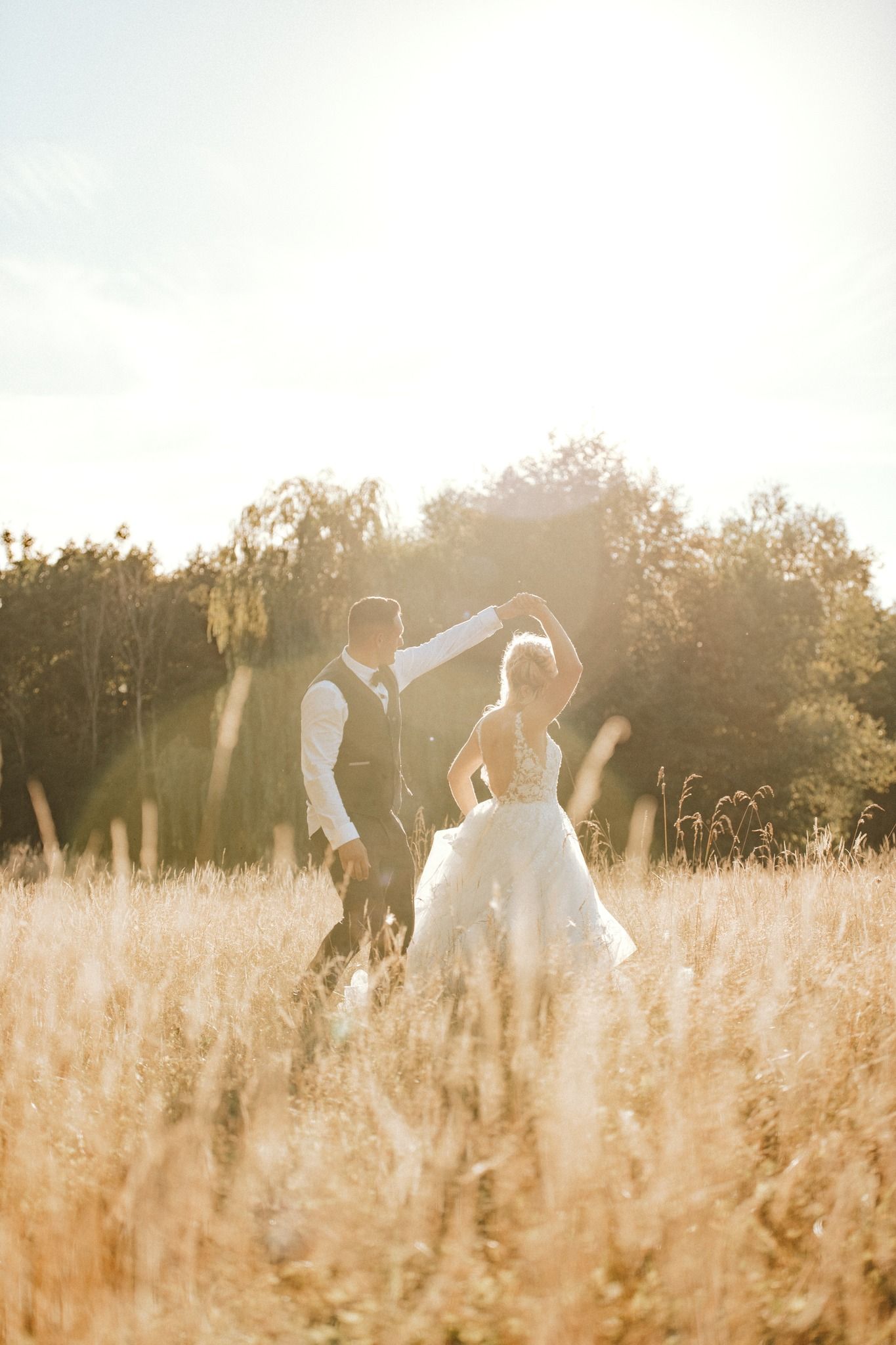 Golden sunlight filters through tall grass as wedding party members walk through a meadow.