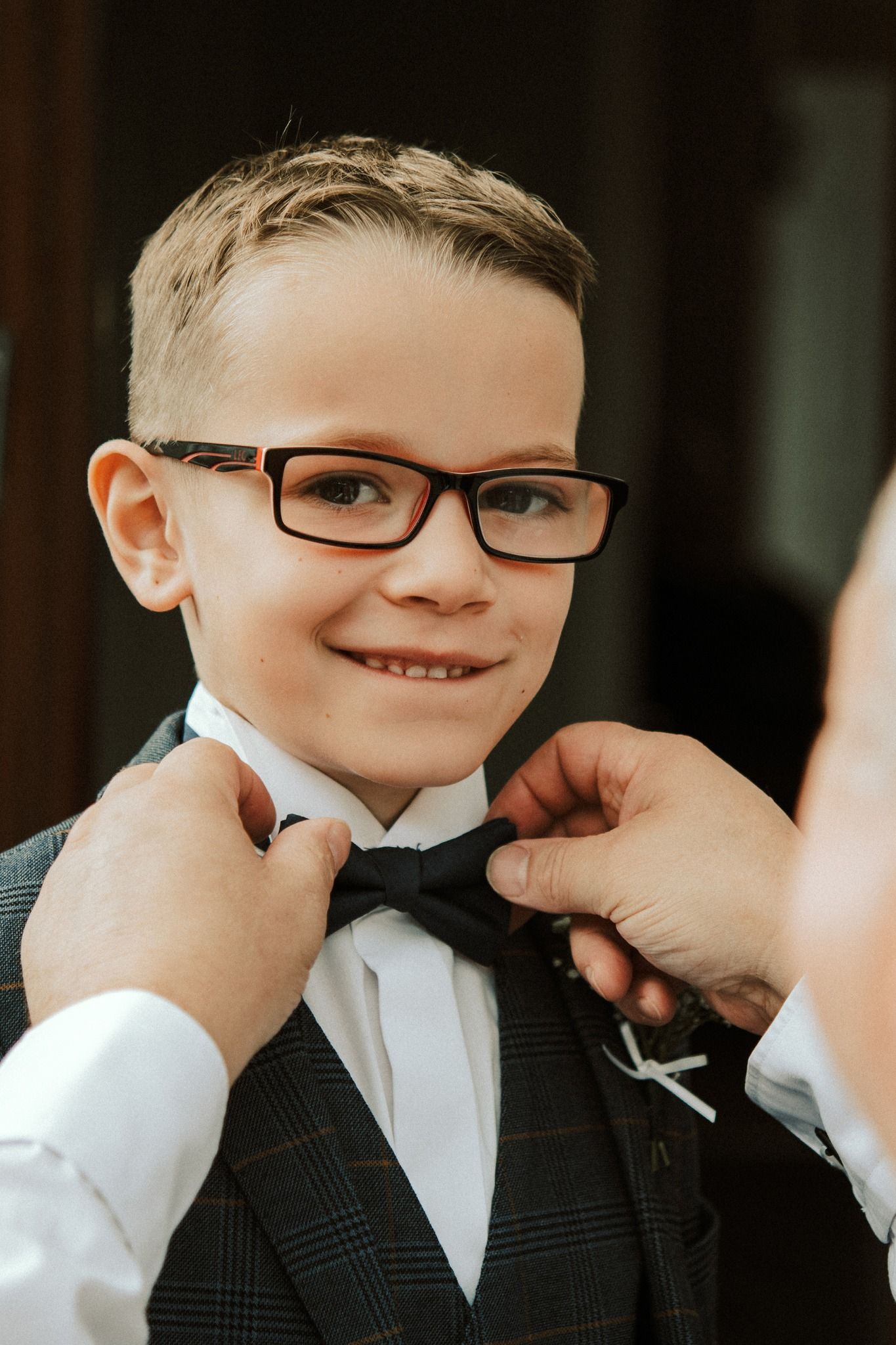 Young ring bearer in formal attire gets his bow tie adjusted.