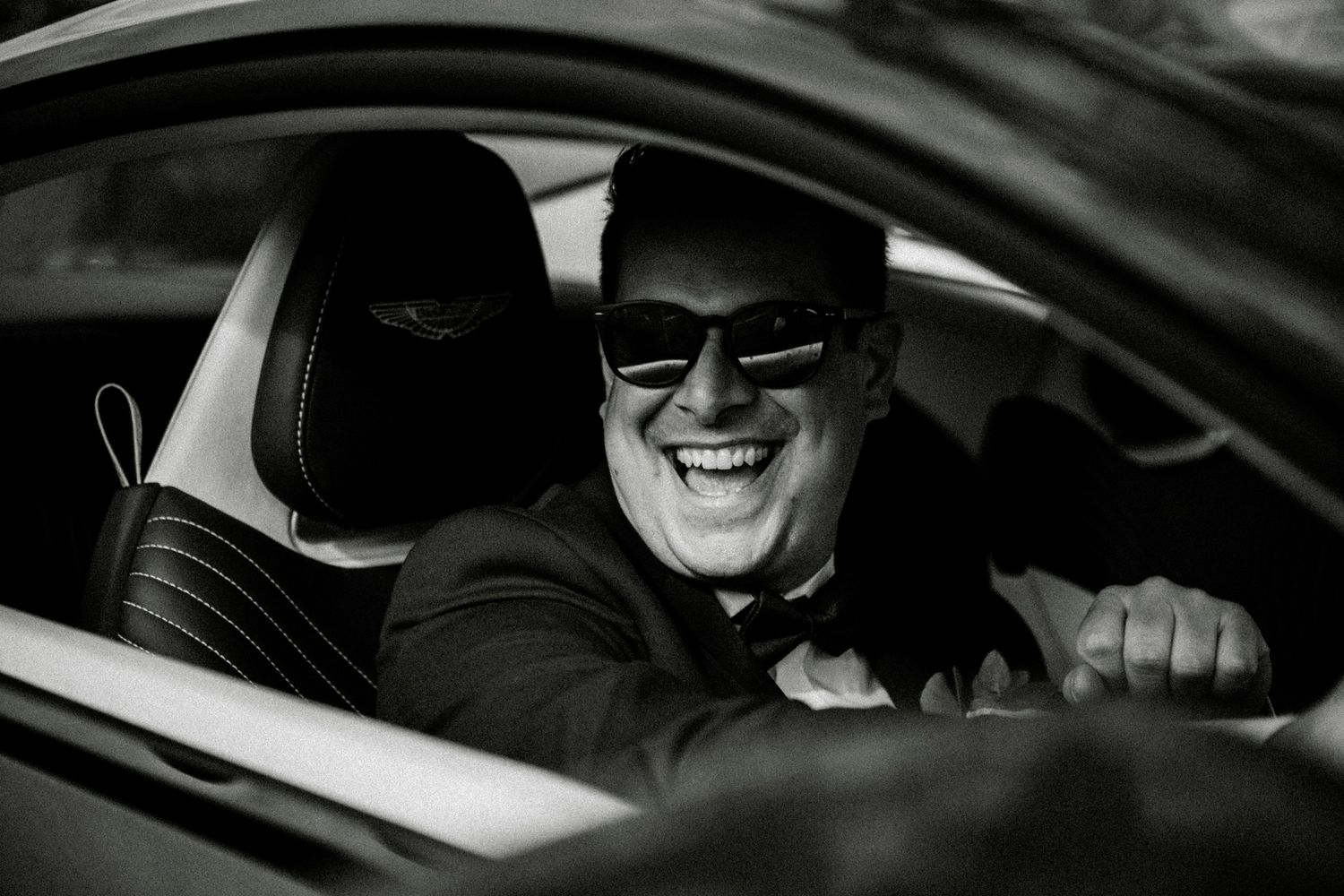 Black and white shot of joyful laughter inside a car on wedding day.