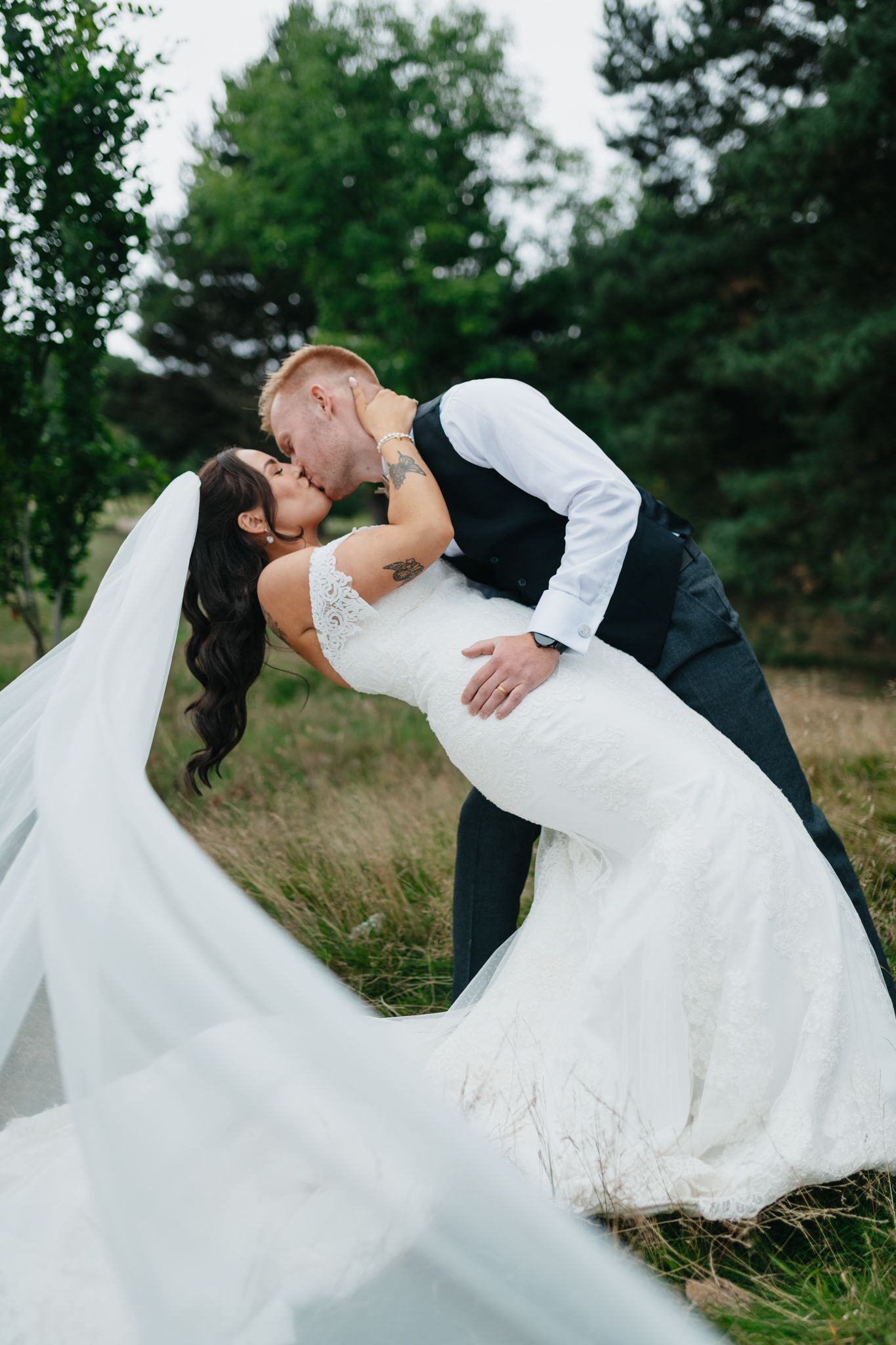 Romantic wedding couple sharing a dip kiss in a scenic field with tall grass and greenery.