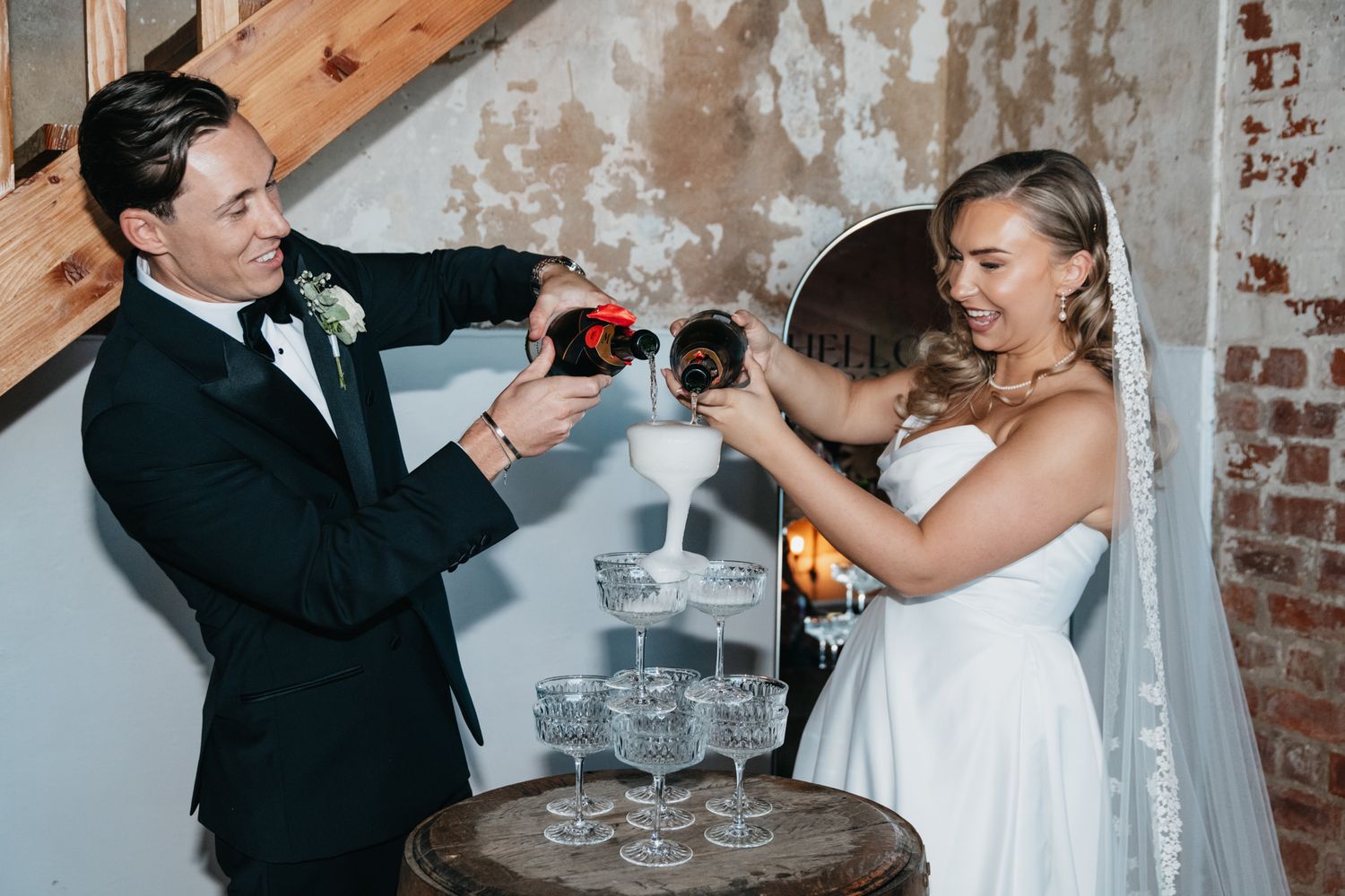Couple hold champagne glasses in joyful toast during celebratory moment at rustic brick venue.