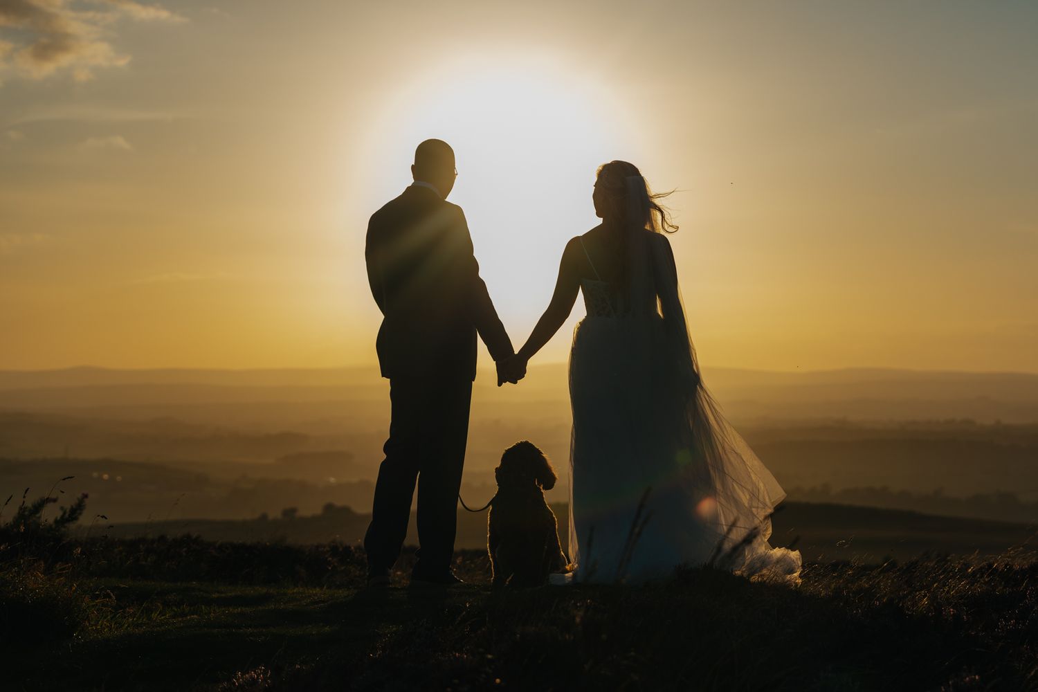 Silhouettes of people holding hands while watching a golden sunset over misty mountains in the distance.