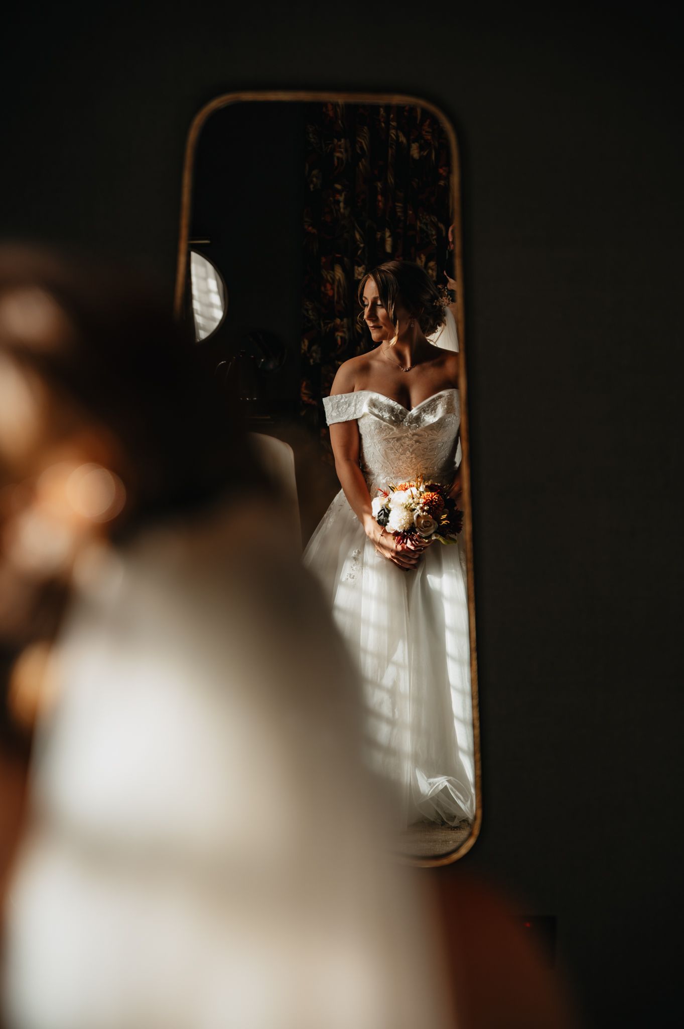 A bride in a white wedding dress holds her bouquet in a dark, moody setting with dramatic lighting.