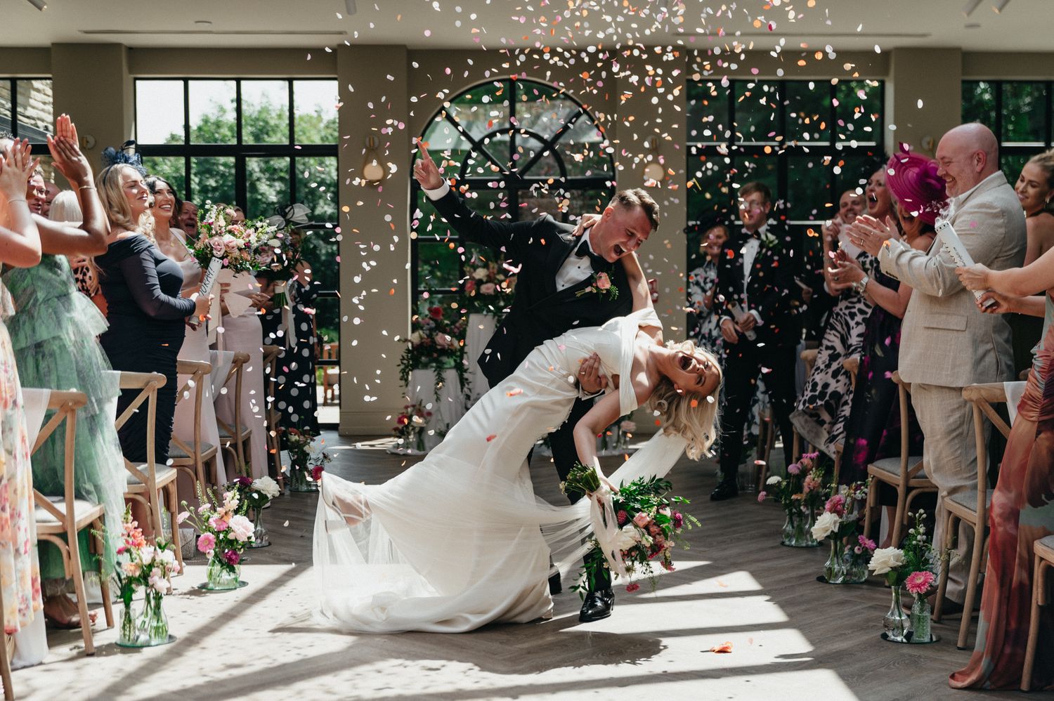Newlyweds share a romantic dip kiss as guests throw confetti during their wedding ceremony exit.