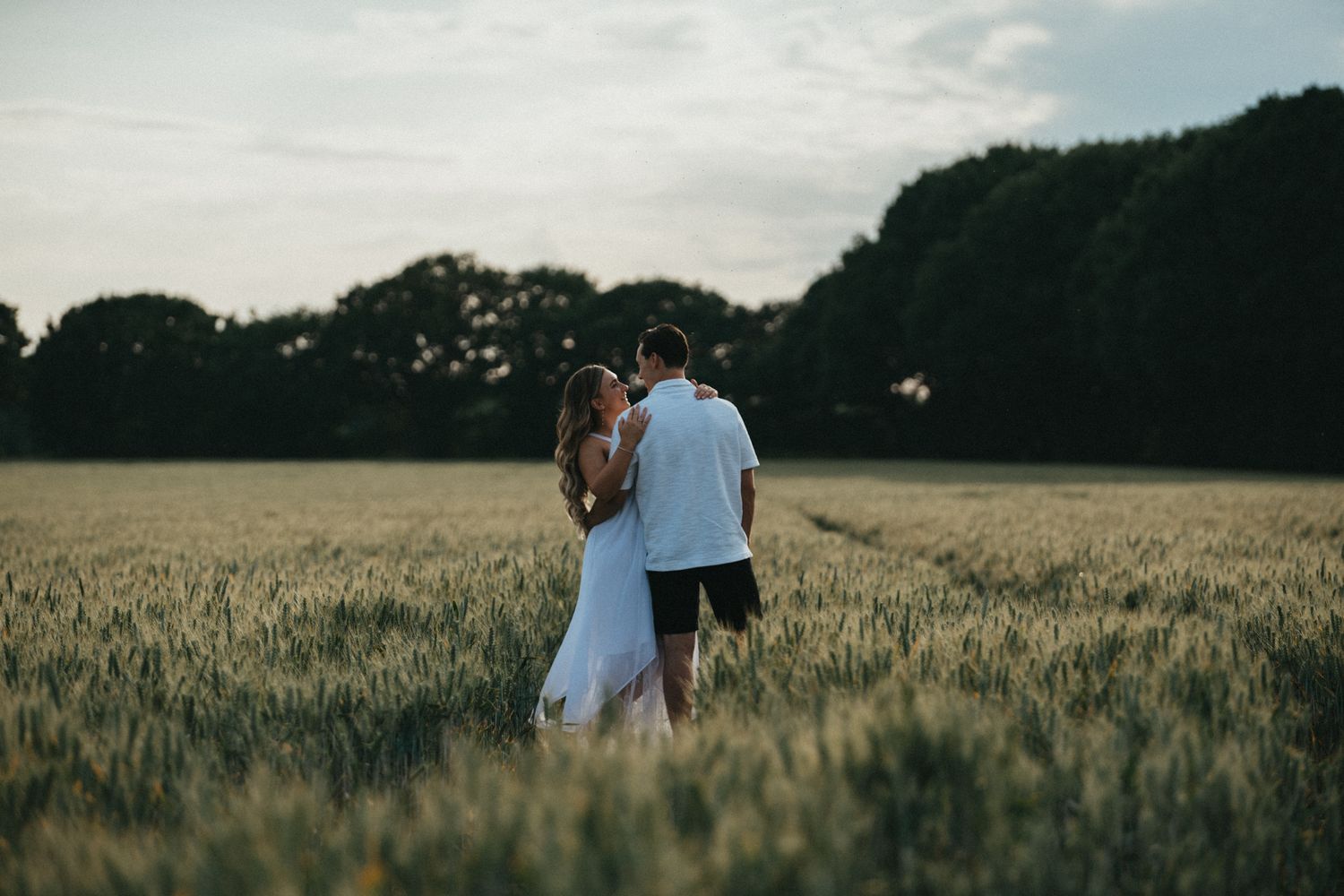 A couple walking together through a golden wheat field at sunset during summer.