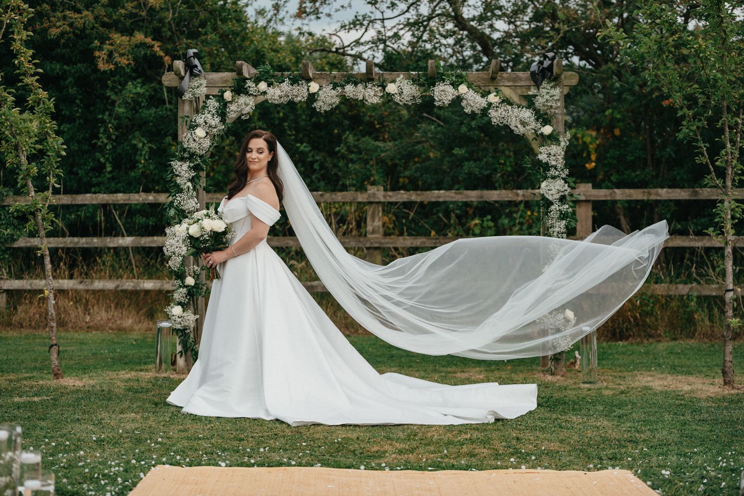 Wedding dress with flowing long train spread out on grass in a garden setting.