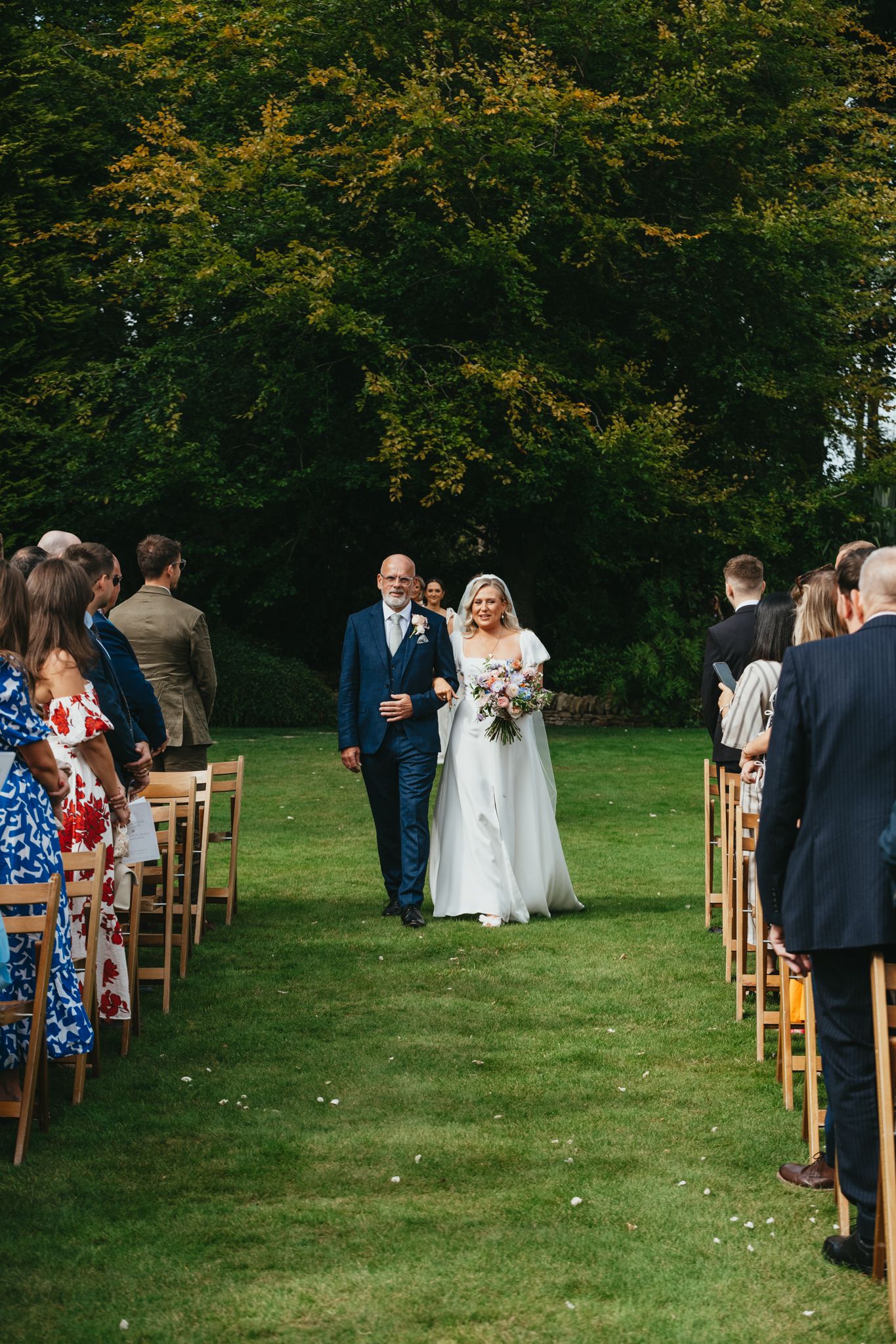 Outdoor garden wedding ceremony setup with wooden chairs and green lawn.