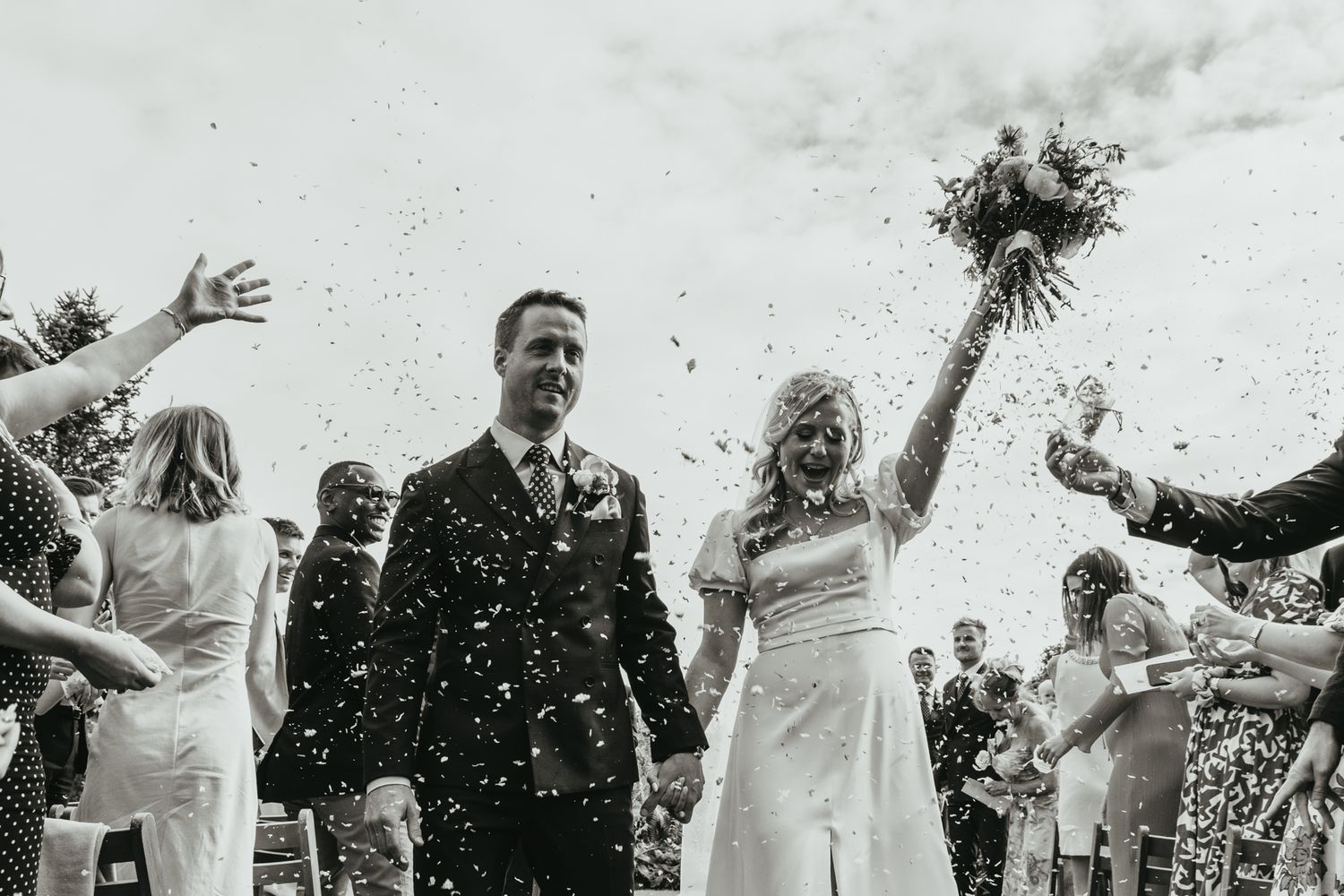 Wedding party celebrating with confetti throws in an outdoor garden setting.