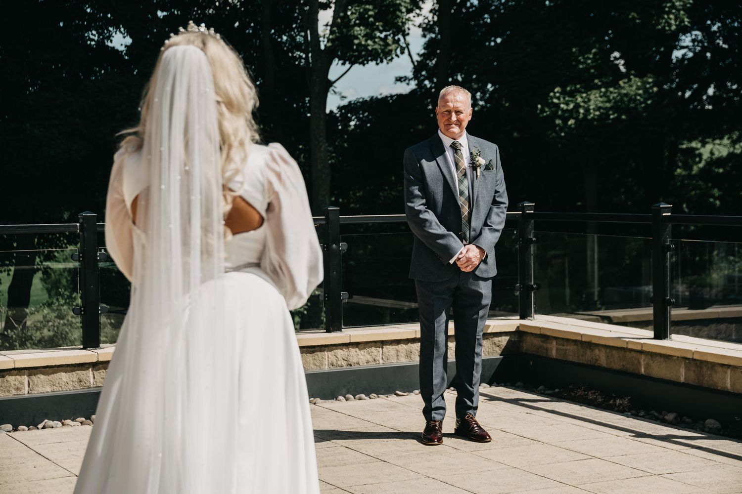 A first look wedding moment on an outdoor terrace with the bride in white and groom in a gray suit.