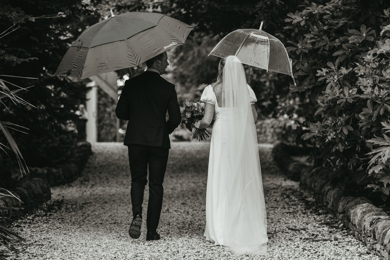Black and white photo of couple walking through garden path on wedding day.