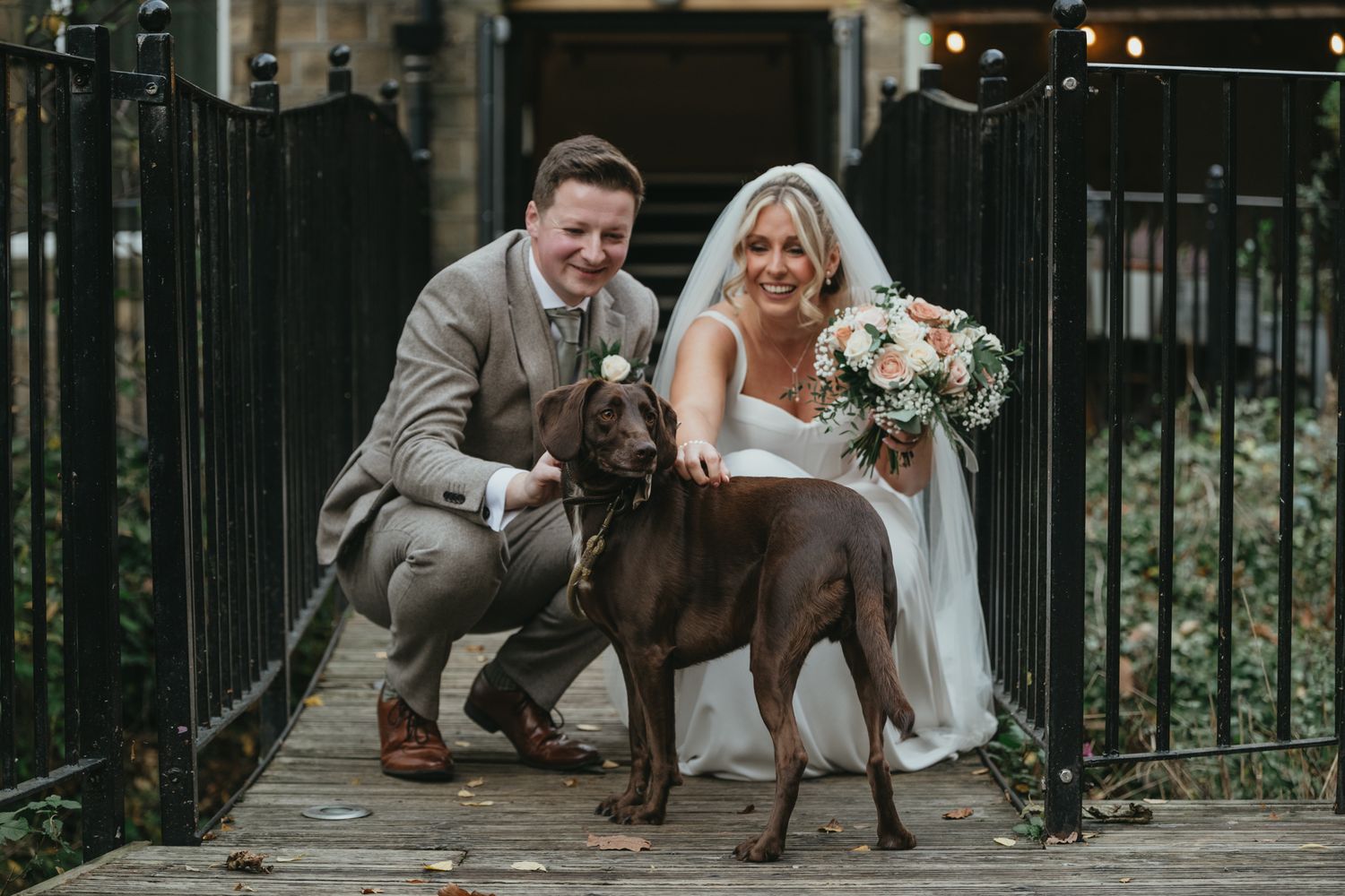 A newlywed couple stands with their brown dog on a rustic wooden deck decorated with potted plants and flowers. The Venue, Halifax