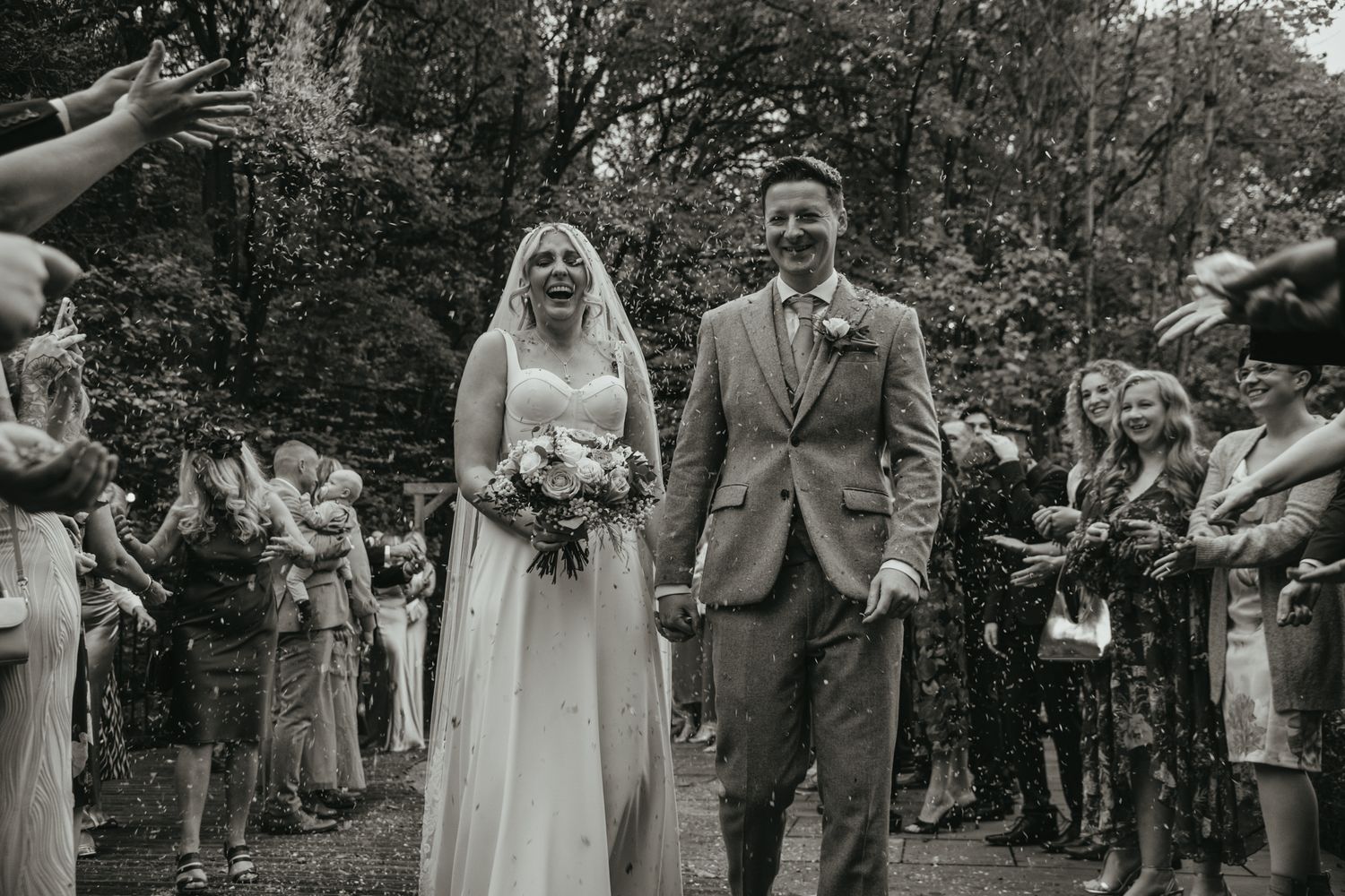 Joyful couple walks down aisle at outdoor woodland wedding ceremony as guests toss flower petals and celebrate. The Venue, Halifax