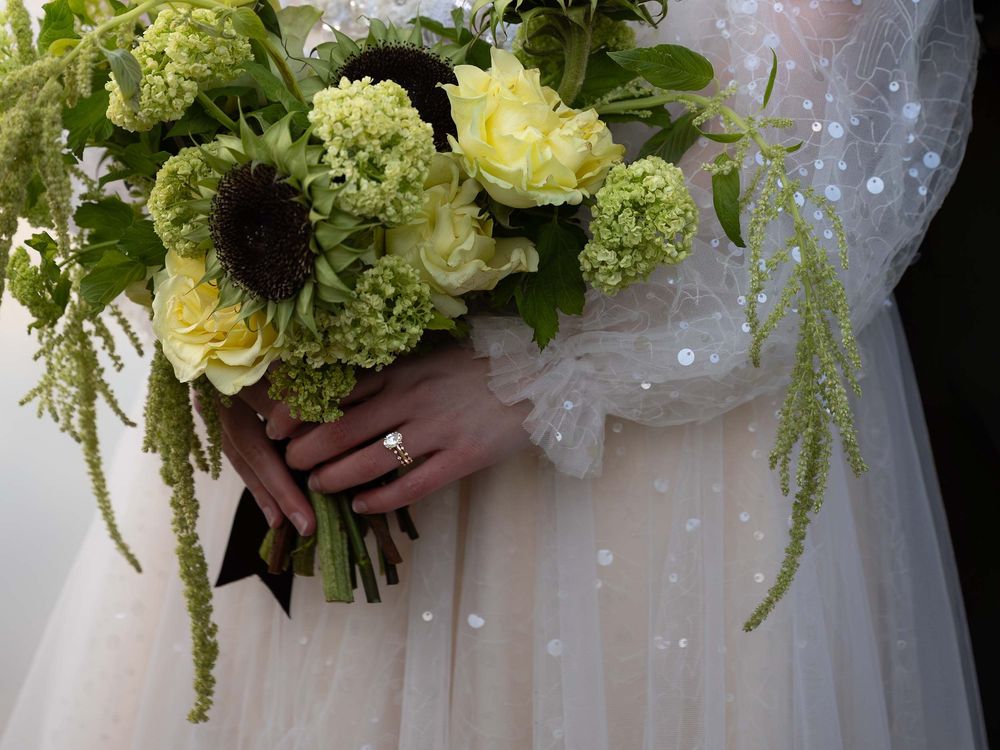 Sharp focus on a bride's wedding rings while she holds her bridal bouquet. The bride wears a blush gown.