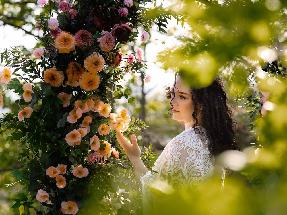 A boho bride reaches toward a flower on a colorful floral arch near Tacoma.