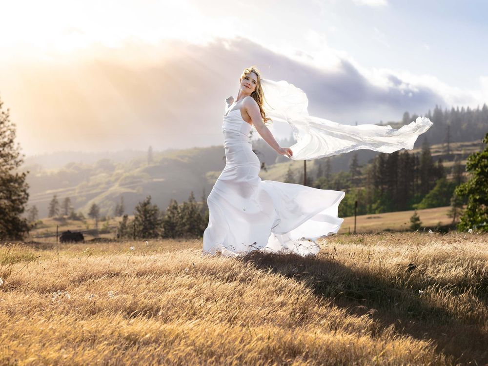 A bride walks in a sunkissed meadow as the wind carries her wedding gown and veil wildly behind her in Southern Washington.