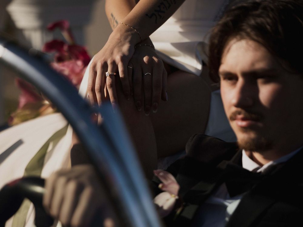 Sharp focus on the bride's engagement ring with her husband at the wheel of the vintage corvette during their PNW elopement.