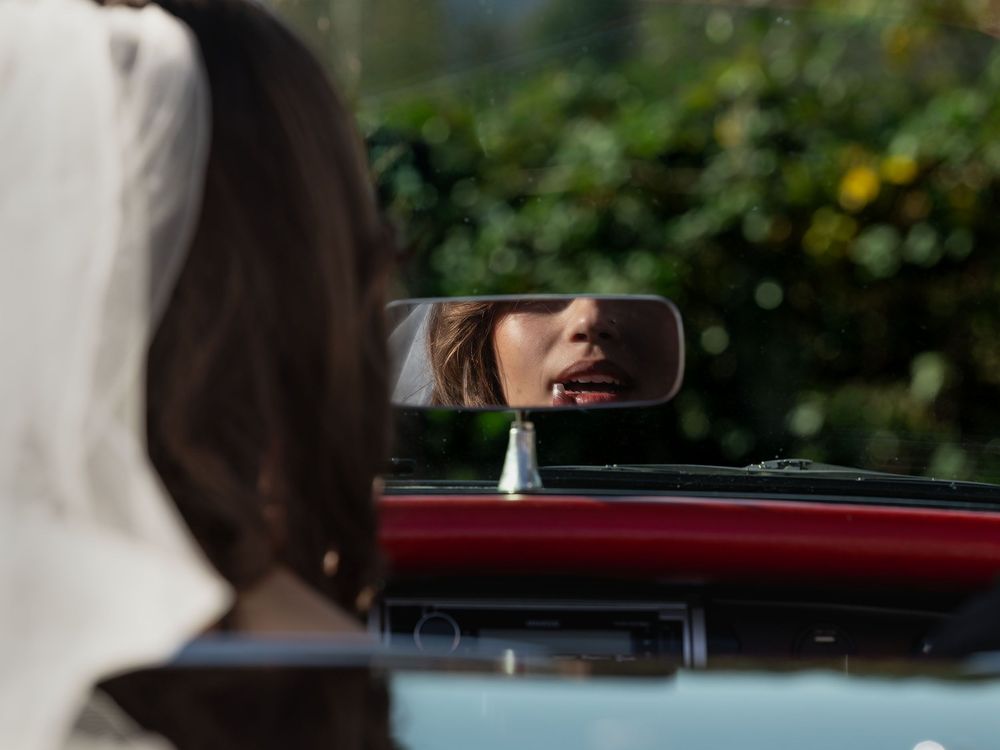 In a high-contrast edit, bride Maddie fixes her lipstick in the rearview mirror of a vintage corvette near Seattle, Washington.