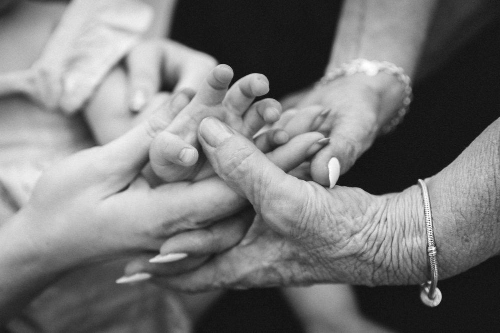 Black and white photo of multiple generations of hands stacked together, symbolizing unity, support, and family connection.