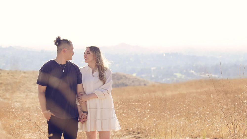 A couple stands together in a golden field during sunset, creating a romantic silhouette against the warm sky.