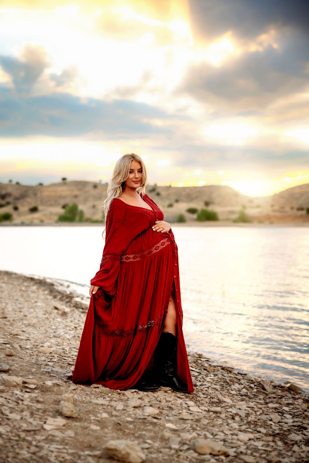 Person wearing flowy red dress poses on sandy beach at sunset against dramatic cloudy sky.