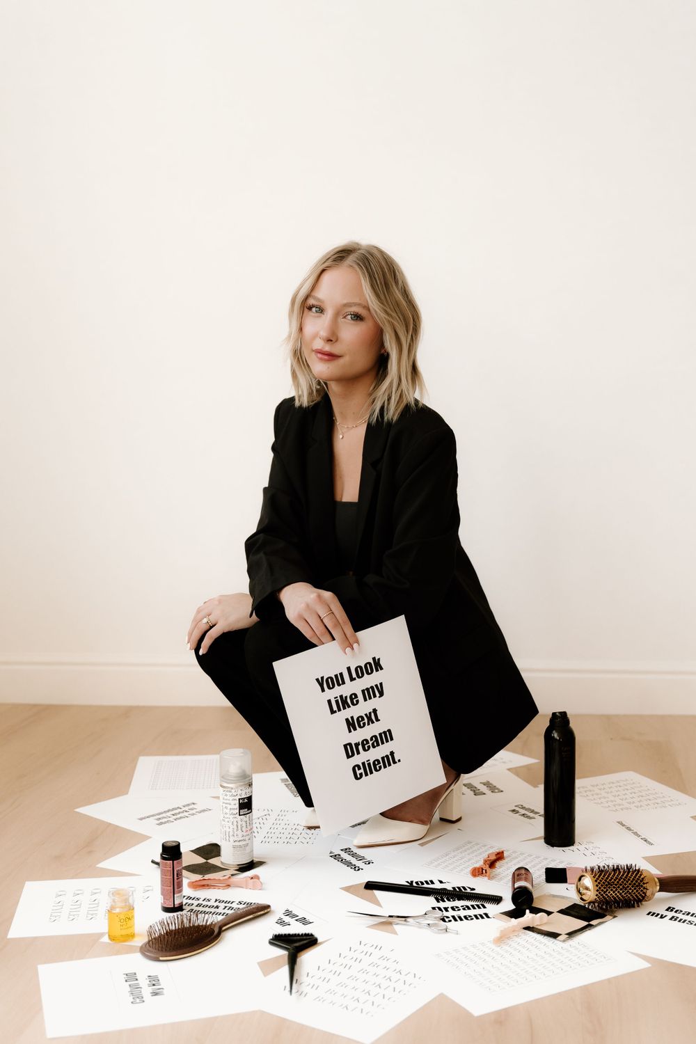 Someone in a black blazer displays artistic materials and typography designs spread across a white floor.