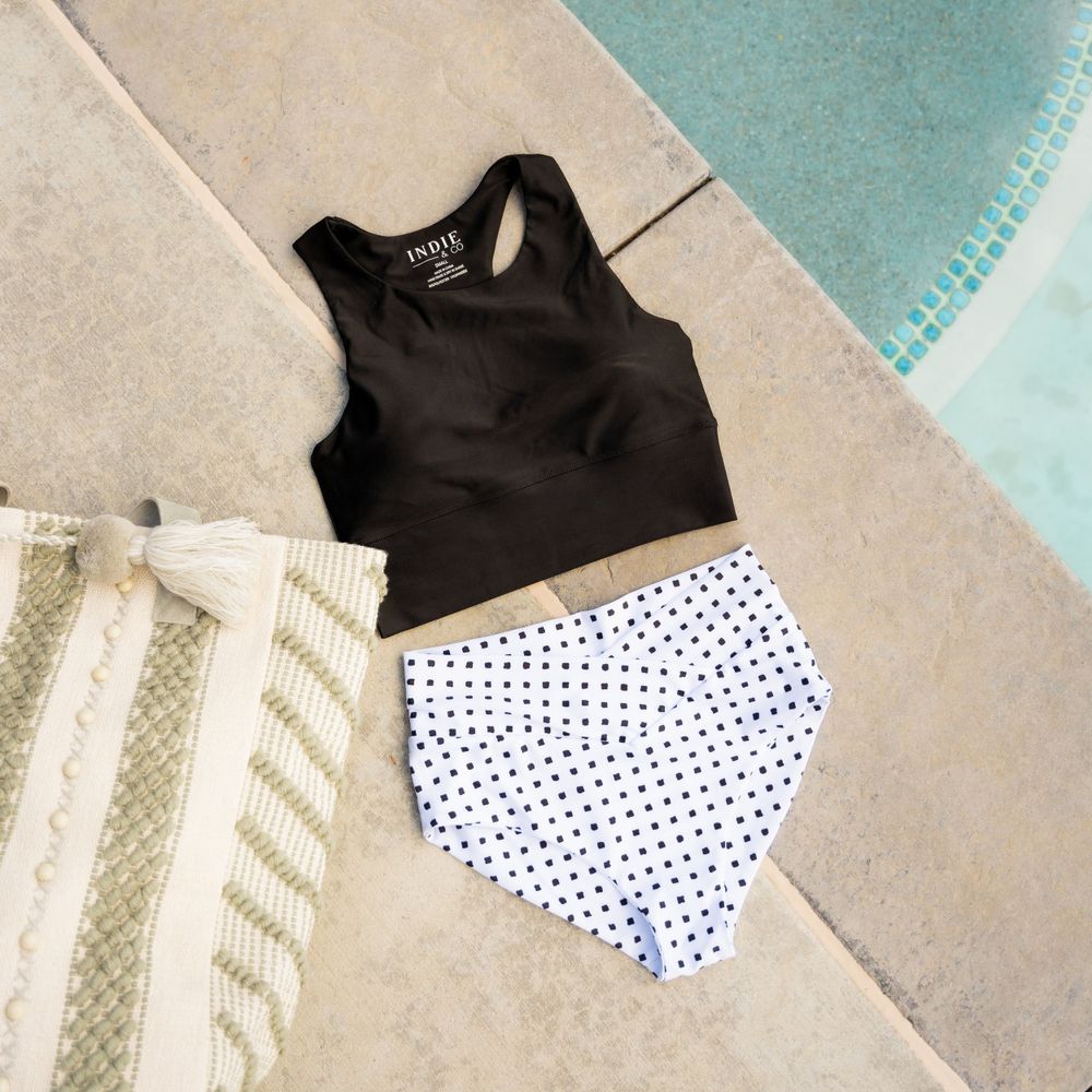 Black racerback top and polka dot bottoms laid flat by pool edge with striped towel.