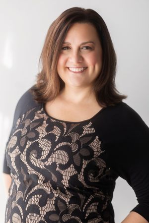 Woman wearing black long sleeve top with beige floral lace pattern against white background.