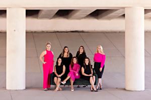 Group portrait with coordinated pink and black outfits against minimalist architectural background.