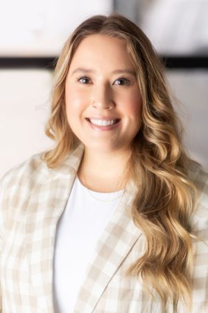 Professional headshot of person in white blazer against neutral background.