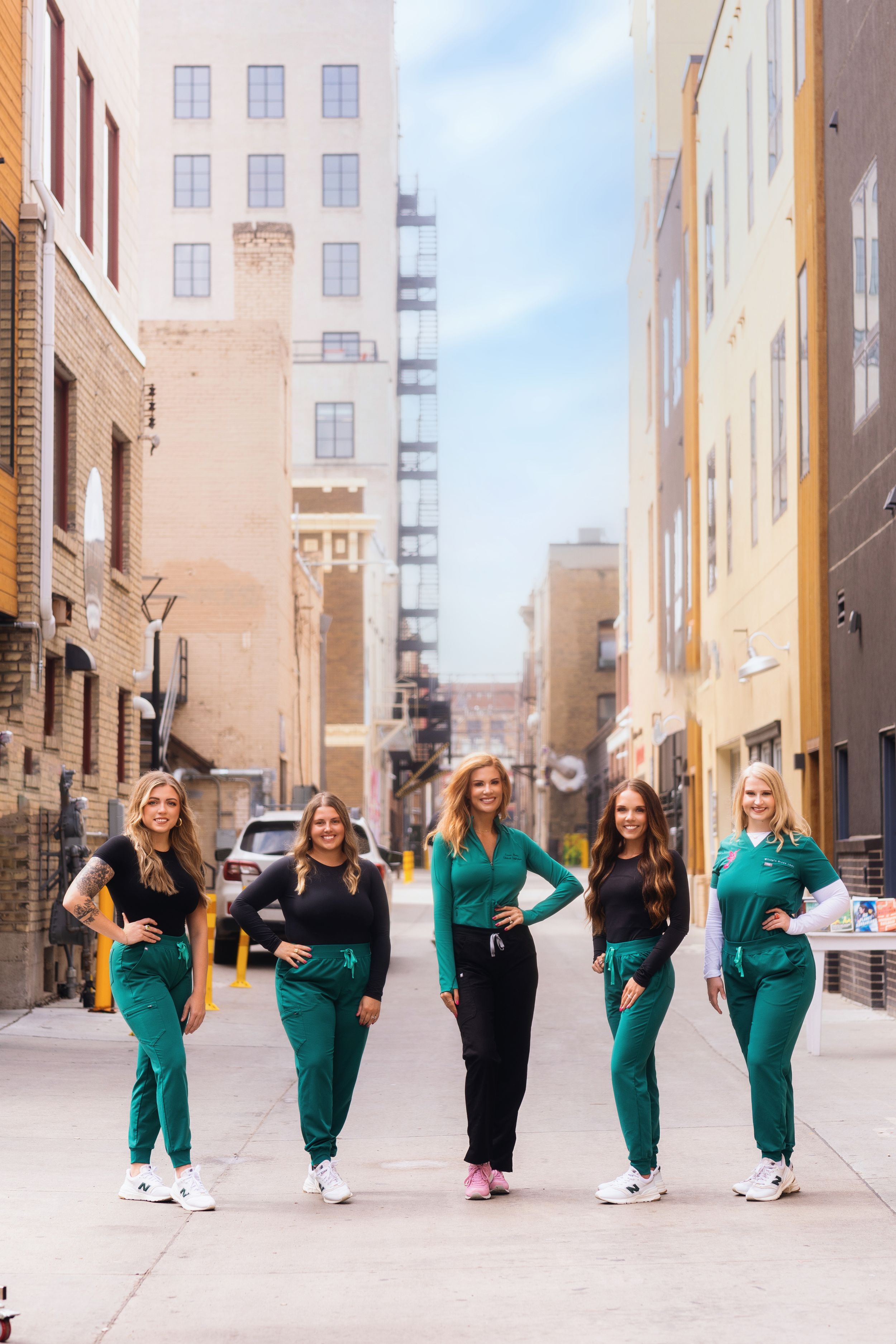 Healthcare workers in matching green scrubs walk together down an urban alley between tall buildings.