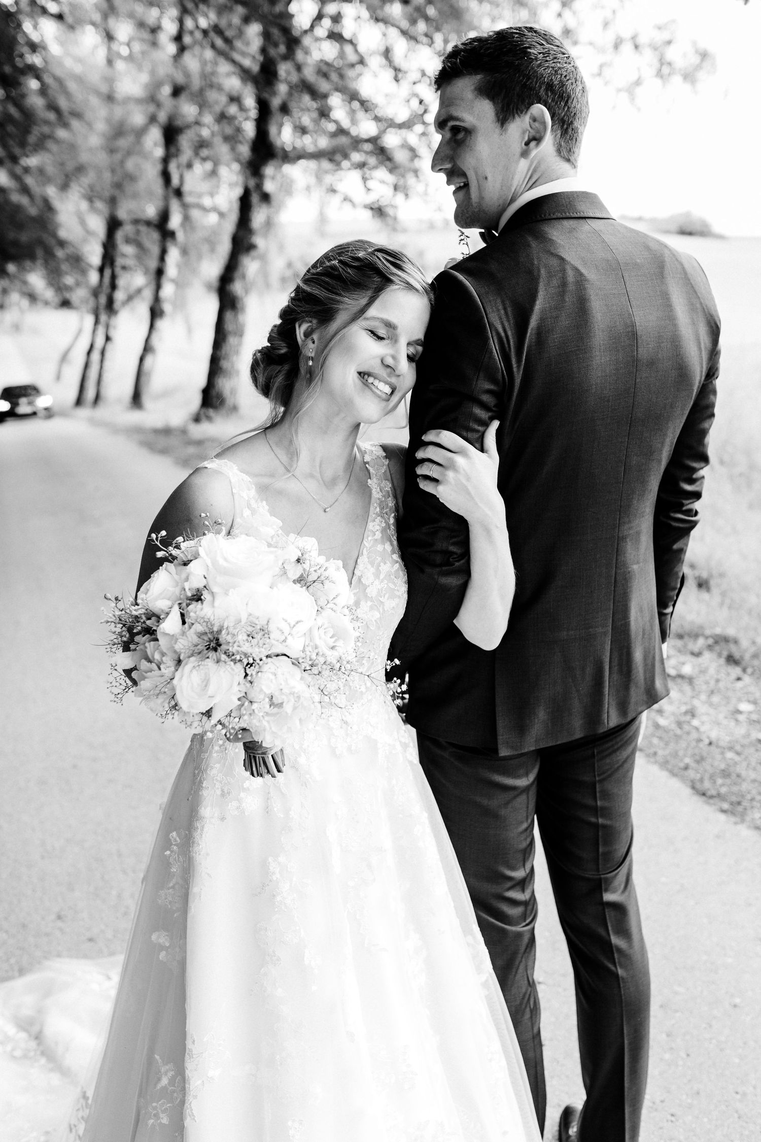 Black and white portrait of newlyweds sharing an intimate moment outdoors with bridal bouquet.