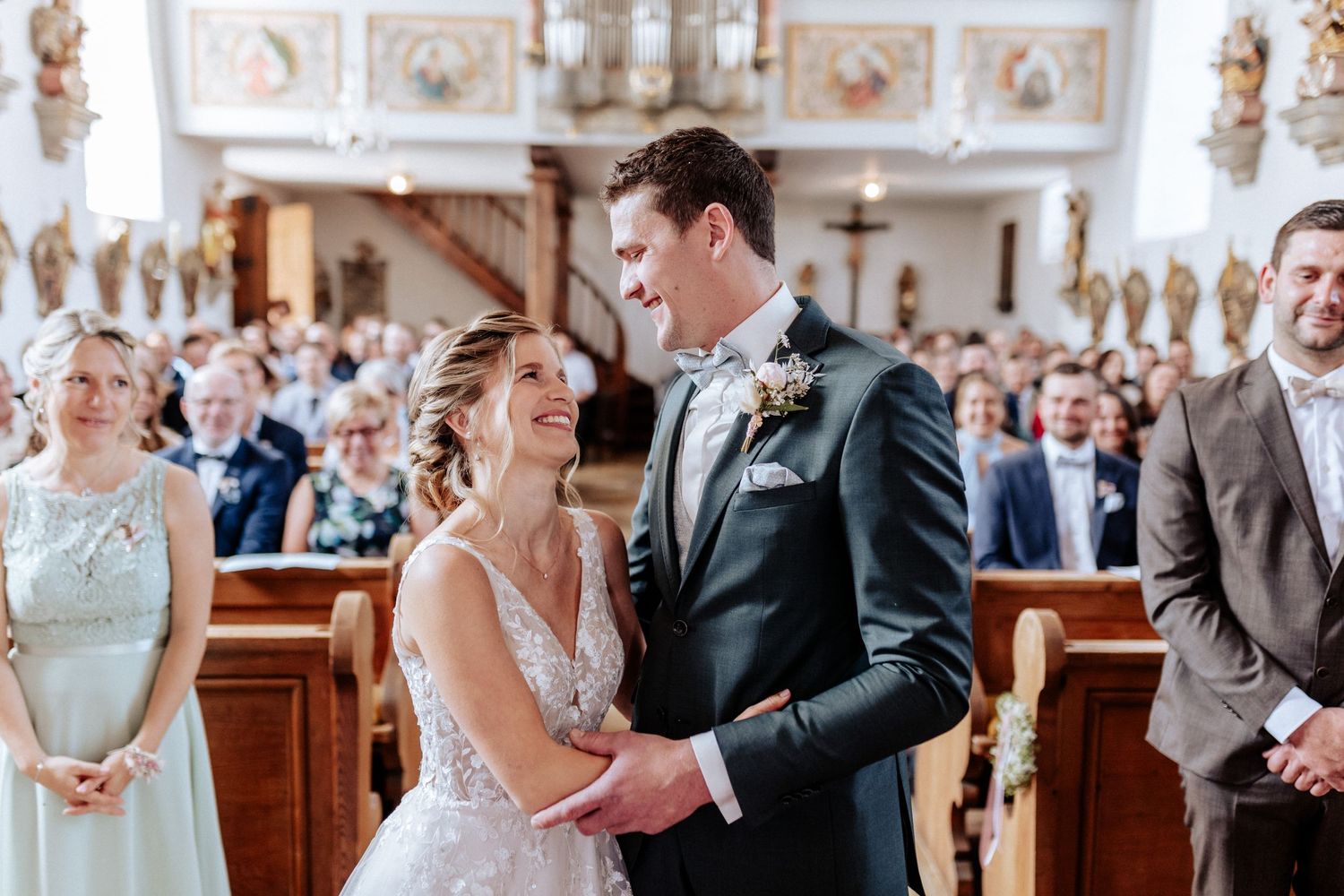 Wedding ceremony in an ornate church with decorative walls and pews filled with guests.