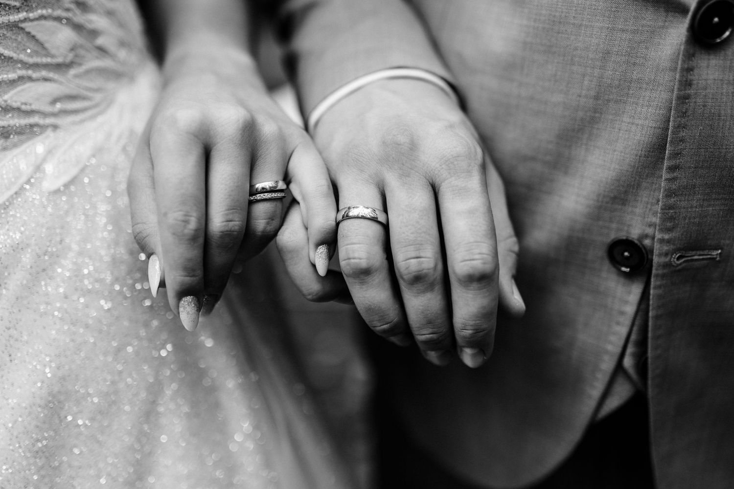 Close-up black and white photo of newlyweds' hands with wedding rings.
