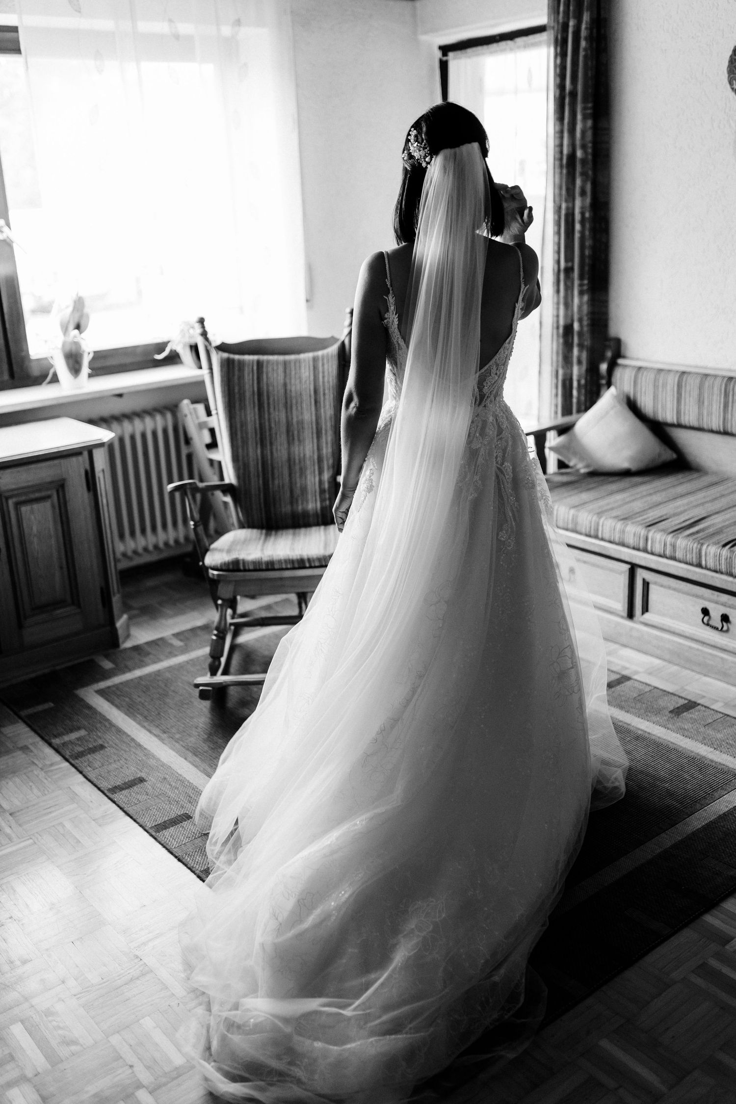 Silhouette of bride in elegant wedding dress and flowing veil standing in room with vintage furniture.
