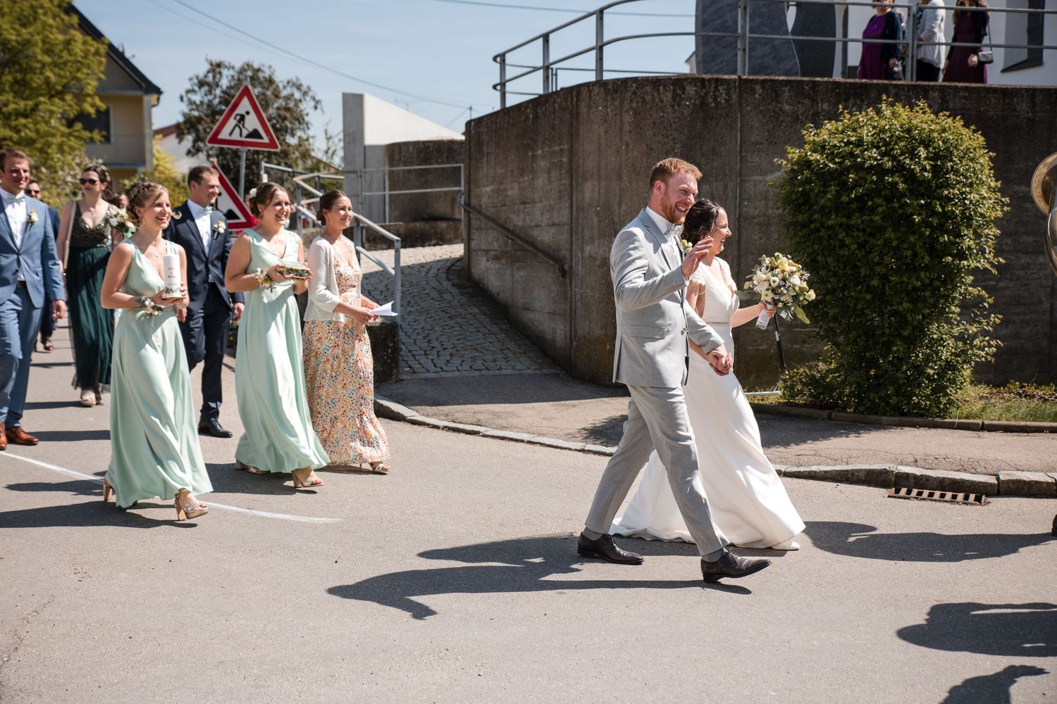 Wedding party in pale blue dresses walking along a sunny pathway.